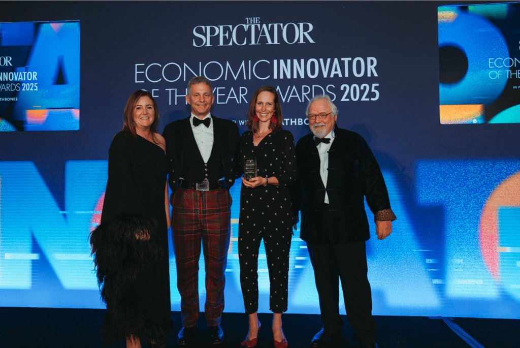 Four people pose on stage at The Spectator’s Economic Innovator of the Year Awards 2025. Rebecca Stewart holds an award trophy beside Duncan Macrae, with the event branding behind them.